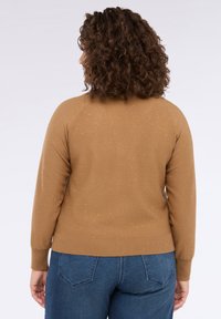 Pulover maro cu o suprafață texturată, având accente subtile de sclipici, mâneci lungi, manșete cu nervuri și un tiv ajustat. Asortat cu blugi albaștri.
