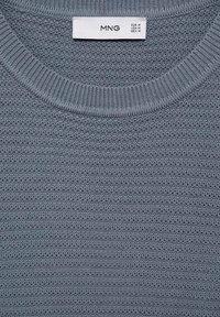 Šedý pletený svetr s texturovaným vzorem. Má žebrovaný kulatý výstřih a štítek s informacemi o velikosti a značce.