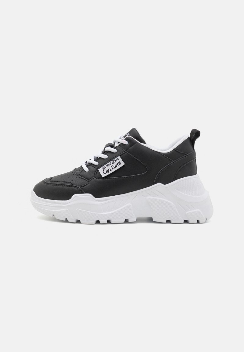Black sneaker with white sole, featuring a padded collar, textured finish, rounded toe, and contrasting black and white laces.