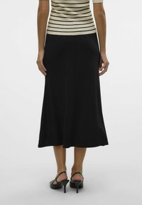 Črna midi krilo z gladko teksturo, razširjeno obliko in subtilnim gibanjem. V kombinaciji s črnimi petami in črtasto majico.