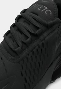 Schwarzer Sportschuh mit strukturiertem Obermaterial, das mit Mesh-Details und auffälliger Schnürung ausgestattet ist. Mit sichtbarem Logo an der Seite.