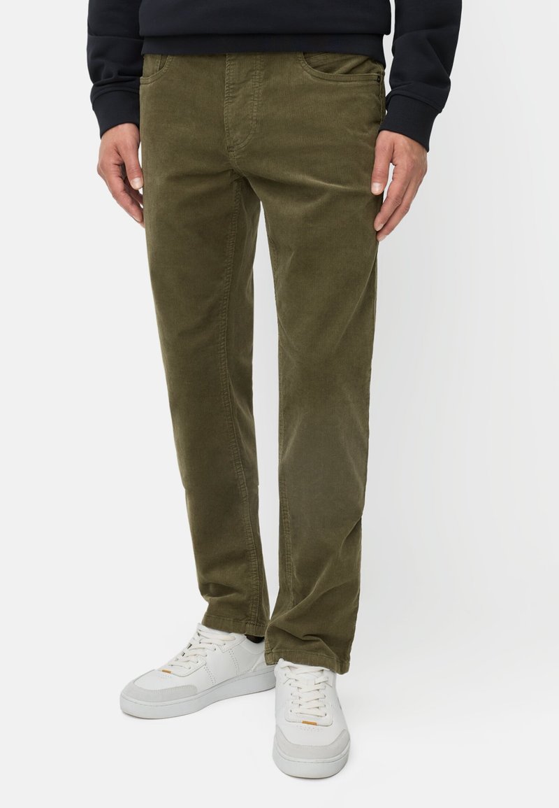 Olivgrüne Cordhosen mit seitlichen Taschen, schmalem Schnitt, strukturiertem Stoff und kombiniert mit weißen Sneakern.