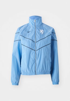 Light blue windbreaker jacket with a high collar, zip closure, black accent lines, and a white lion logo on the chest. Elastic cuffs.