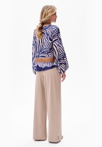 Bluse mit Zebra-Muster in Blau und Beige, mit voluminösen Ärmeln, kombiniert mit beigen weiten Hosen. Glatter Stoff und lässige Passform.