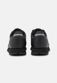Svarta Reebok-sneakers med en slät läder- och meshyta, vadderad häl och strukturerad gummisula. Logotypen är tydligt synlig på hälen.