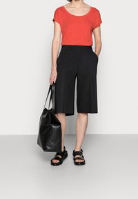 Rød kortærmet top, sorte vide shorts, sort læder tote taske, og sorte sandaler med justerbare stropper. Glatte teksturer hele vejen igennem.