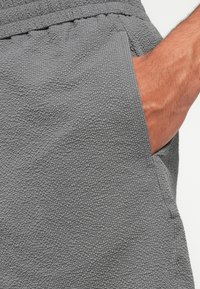 Gray textured shorts featuring a pocket on the side and a waistband with a gathered finish. The fabric has a soft, tactile surface.