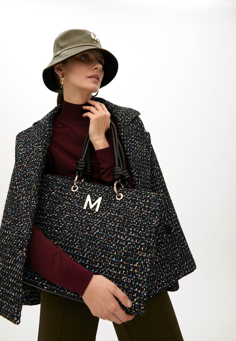 Kabelka z tvídu s černým a multikolorovým tkaním, zlatým kováním a černými uzlovými rukojeťmi; nošena s vínovým rolákem a vzorovaným kabátem.