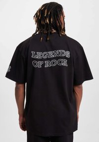 Juodas perteklinio dydžio marškinėliai su ryškiu baltu tekstu "ROCA LEGENDOS" ant nugaros. Trumpomis rankovėmis ir laisvu siluetu. Minkšta medvilnės tekstūra.