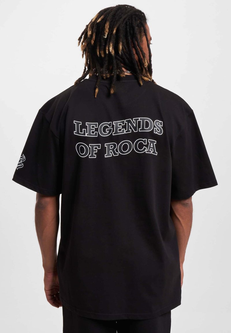 Juodas perteklinio dydžio marškinėliai su ryškiu baltu tekstu "ROCA LEGENDOS" ant nugaros. Trumpomis rankovėmis ir laisvu siluetu. Minkšta medvilnės tekstūra.