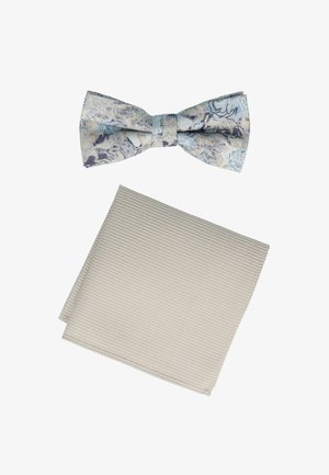 Ein blau-weiß gemusterter Fliegenriemen auf einem strukturierten beigefarbenen Taschentuch. Beide Gegenstände weisen elegante Stoffdesigns auf.