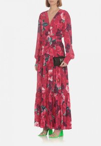 Lungo vestito floreale di un rosa vivace con accenti verdi e bianchi, caratterizzato da scollo a V, bottoni e una gonna a strati. Abbinato a una pochette nera e tacchi verdi.