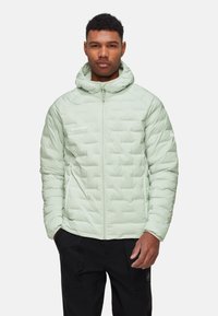 Hellgrüne isolierte Jacke mit Kapuze, mit gestepptem Design und Frontreißverschluss, getragen über einer schwarzen Hose. Markenlogo gut sichtbar.