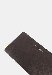 Portafoglio in pelle marrone texturizzato con finitura liscia, caratterizzato da un logo dorato, forma allungata e dettaglio della zip.