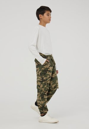Pantaloni cargo camouflage in verde e marrone, realizzati in tessuto morbido. Presentano tasche laterali, vita con cordino e polsini elasticizzati. Abbinati a sneakers bianche.