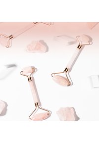 Rosenkvarts ansiktsrullere med gullhardware, med glatte rosa steiner i ovale og runde former på en hvit bakgrunn.