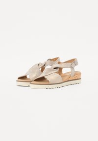 Sandales crossover beiges avec une finition scintillante, bout ouvert et talon en liège avec une semelle en caoutchouc. Sangle de cheville réglable incluse.