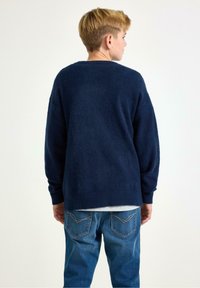 Mørkeblå crewneck-trøje med blød, tekstureret finish, båret af en person iført lyseblå jeans, set bagfra.