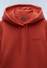 Rostfarbener Kapuzenpullover aus weichem, strukturiertem Stoff. Besitzt eine vordere Kängurutasche und ein kleines Logo auf der Brust.