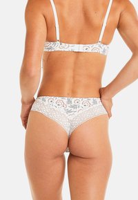 Sous-vêtements hipster en dentelle blanche avec des motifs floraux en gris et rouge. Présente un bord festonné et des bretelles réglables sur le soutien-gorge assorti.