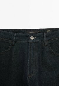 Mörkblå denimjeans med en tapered passform. Har en metallknapp, kontrasterande sömmar och fickor fram och bak.