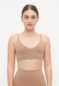 Nude seamless bralette with a soft, smooth texture, V-neck design, adjustable straps, and a wide underband for support.