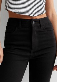 Black high-waisted jeans with a smooth texture, front button closure, and side pockets. Paired with a cropped striped top.