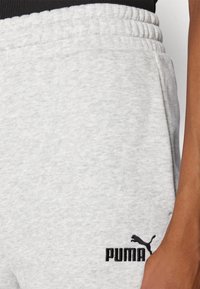 Pantalons de survêtement gris en tissu doux, avec une taille élastique et des poches latérales, ornés d'un logo Puma noir brodé sur la jambe.