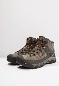 Graue Wanderschuhe mit strukturierten Oberflächen, orangefarbenen Schnürsenkeln und Gummisohle. Mit verstärkter Zehenkappe, gepolstertem Knöchel und Logo-Akzent.