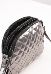 Borsa a mano metallizzata argentata trapuntata con due compartimenti con zip, fodera interna nera e dettagli in metallo argentato. Forma rettangolare compatta.