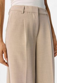 Beige op maat gemaakte broek van lichtgewicht stof, met voorplooien en zijzakken, met een soepele textuur en gestructureerd ontwerp.