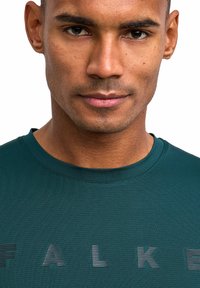 Ciemnozielona sportowa koszulka z teksturowanej tkaniny, z okrągłym dekoltem i subtelnym logo w paski nadrukowanym na piersi.