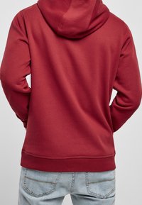 Sweat à capuche bordeaux avec capuche à cordon, poignets et ourlet côtelés ; associé à un jean bleu clair avec détails de couture sur les poches arrière.