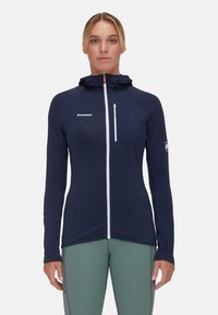 Granatowa kurtka z kapturem na pełny zamek, z długimi rękawami, kieszenią na piersi i akcentami z logo. Wykonana z lekkiej, teksturowanej tkaniny.