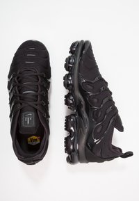 Zwarte sportieve schoenen met een glad, textuur bovenwerk, opvallende demping en een glanzende zwarte rubberen zool met ronde noppen.