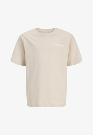 Dreng stående, iført sort og hvid blomster kortærmet skjorte, beige T-shirt, blå jeans og hvide sneakers, kigger mod højre.