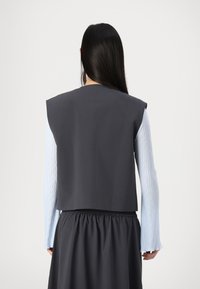 Gray sleeveless top featuring a structured design, paired with a long-sleeve light blue ribbed shirt and a gathered waist black skirt.