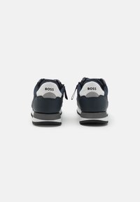 Scarpe da ginnastica blu navy con accenti bianchi e grigi, caratterizzate da una tomaia testurizzata, punta rotonda e chiusure con zip sui lati.