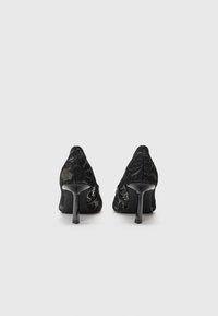 Pantofi cu toc înalt din dantelă neagră, cu vârf ascuțit și toc subțire de tip stiletto, având modele florale și un design semi-transparent.