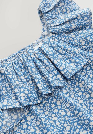 Blå blomstret bluse med hvide mønstre, der har flæser på ærmerne og et struktureret stof. Designet inkluderer detaljerede blomstermotiver.