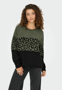 Sweter dzianinowy z zielonym wzorem w panterkę, czarną dolną częścią, okrągłym dekoltem i luźnym krojem. Tekstura materiału z długimi rękawami.