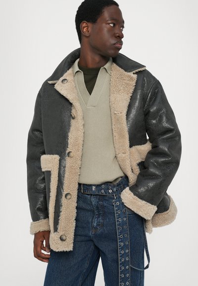 Jachet�ă din piele neagră cu interior din blană bej, cu guler mare, închidere cu nasturi și buzunare laterale. Denim bleumarin cu accente din inele.