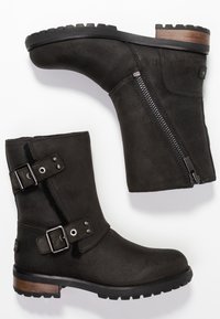 Černé kotníkové boty vyroben�é z texturované kůže mají boční zip, dva nastavitelné popruhy s přezkami a odolnou gumovou podrážku s dřevěným akcentem.