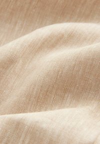 Vaalean beige kangas, jossa on teksturoitu kudonta ja hienovaraisia sävyn vaihteluita. Materiaali vaikuttaa pehmeältä ja kevyeltä, ja siinä on sileä pinta.
