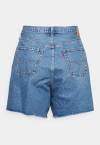 Shorts de mezclilla azul con dobladillos deshilachados, dos bolsillos traseros, trabillas para cinturón y una pequeña etiqueta roja en el bolsillo derecho.
