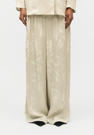 Béžové široké nohavice s jemným kvetinovým vzorom, nosené s béžovým sakom a čiernymi topánkami so špičkou, celotelový pohľad.