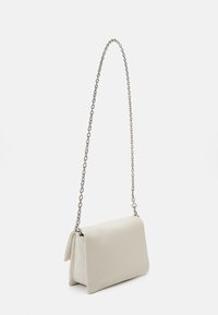 Malá béžová kabelka na rameno s dlouhým stříbrným řetízkovým popruhem a obdélníkovou klopnou, vystavená na bílém pozadí.