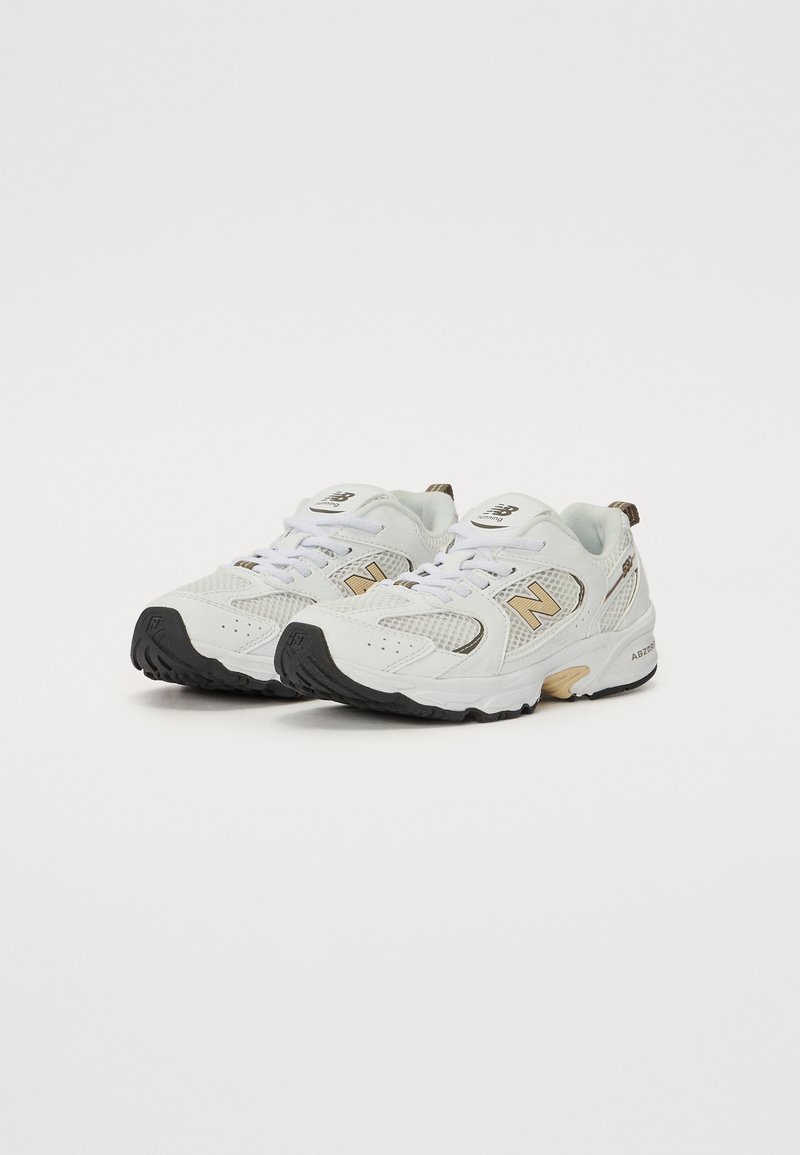 Witte sportieve schoenen met bovenwerk van mesh en synthetisch materiaal, met beige accenten, zwarte rubberen zool en veters. Logo op de zijkant en de tong.