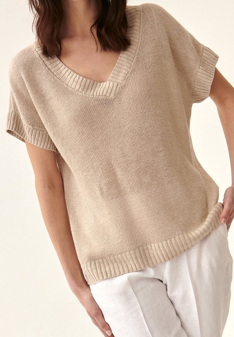 Maglione beige in maglia con scollo a V, maniche corte e tessuto strutturato. Orlo e bordi delle maniche a coste per una finitura dettagliata.