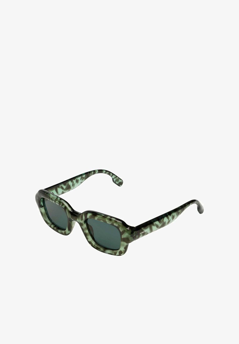 Gafas de sol cuadradas con un patrón de camuflaje en verde y negro. Lentes oscuros y montura de plástico grueso y brillante. Con detalles de marca en la patilla.